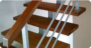 Escalera con estructura de metal color aluminio, pasos de madera pumaquiro con acabado DD brillante. Pasamanos de madera cedro